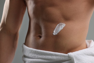 Man with moisturizing cream on his body against grey background, closeup