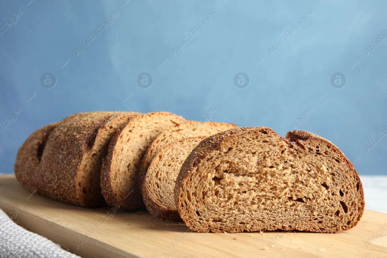 Photo of Tasty sliced bread on wooden board against color background