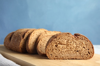 Tasty sliced bread on wooden board against color background