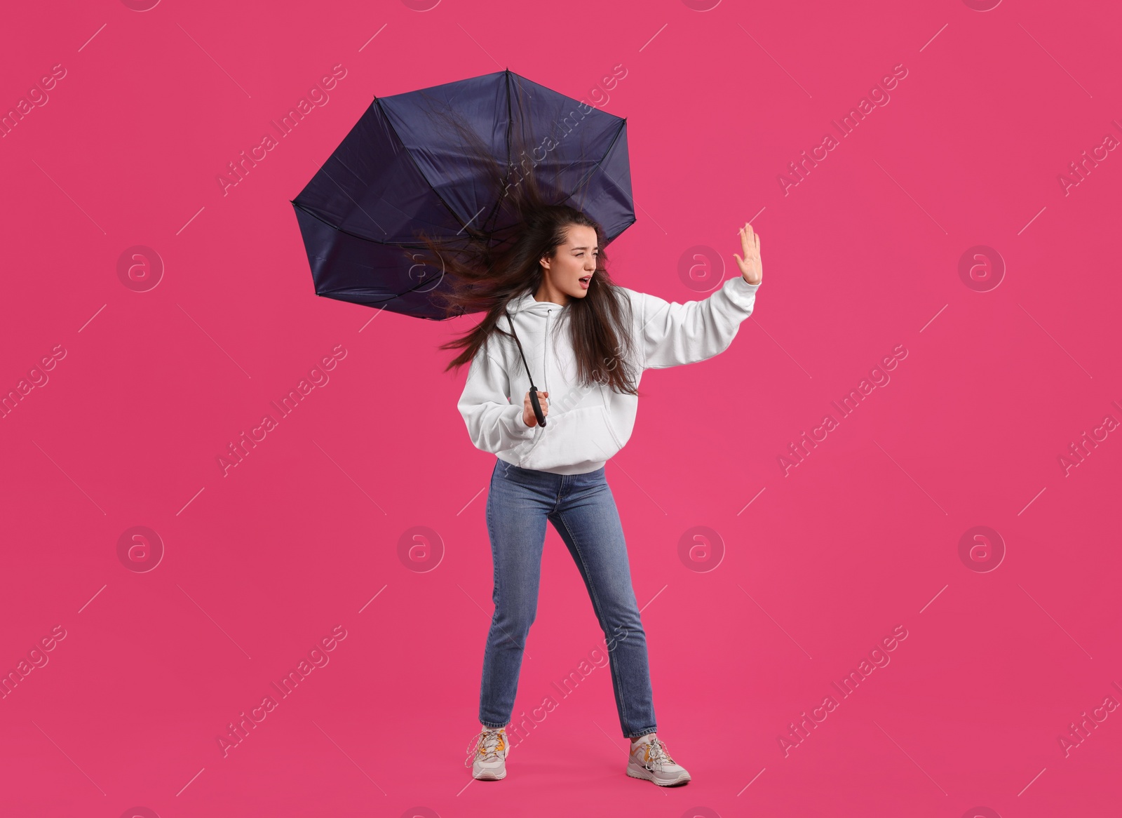 Photo of Emotional woman with umbrella caught in gust of wind on pink background