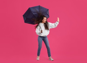 Photo of Emotional woman with umbrella caught in gust of wind on pink background