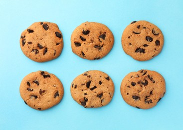 Many delicious chocolate chip cookies on light blue background, flat lay