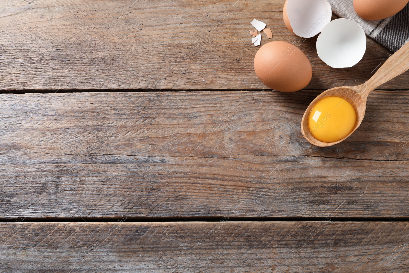 Photo of Raw chicken eggs and spoon with yolk on wooden table, flat lay. Space for text
