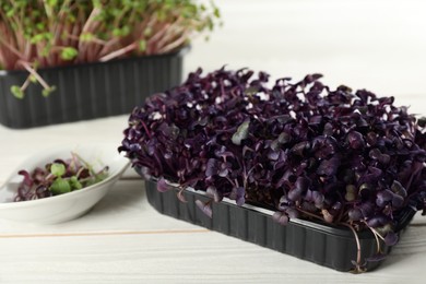 Photo of Fresh radish microgreens in plastic container on white wooden table, closeup