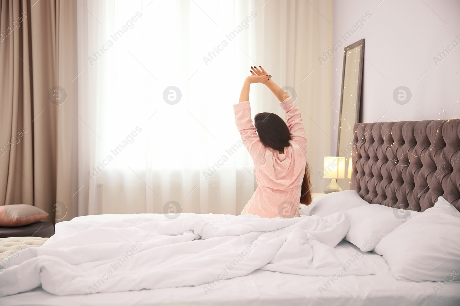 Photo of Young woman stretching on bed in hotel room