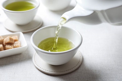 Photo of Pouring green tea into white porcelain cup on light table