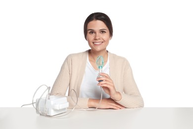 Photo of Happy young woman with nebulizer at table on white background