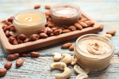 Photo of Different types of delicious nut butters and ingredients on light blue wooden table, closeup