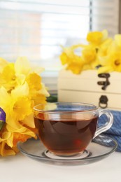 Cup of aromatic tea and beautiful yellow daffodil on windowsill. Space for text