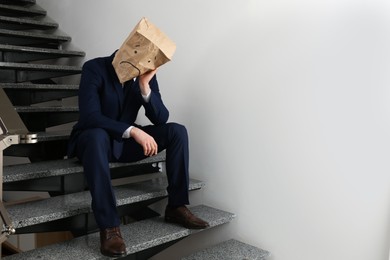 Photo of Man wearing paper bag with drawn sad face indoors. Space for text