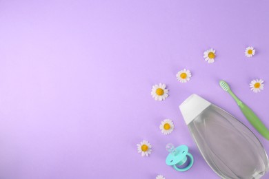 Photo of Bottle with baby oil, pacifier and toothbrush near daisies on violet background, flat lay. Space for text