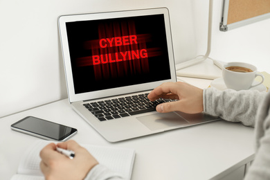 Young man using laptop at white table, closeup. Cyber bullying