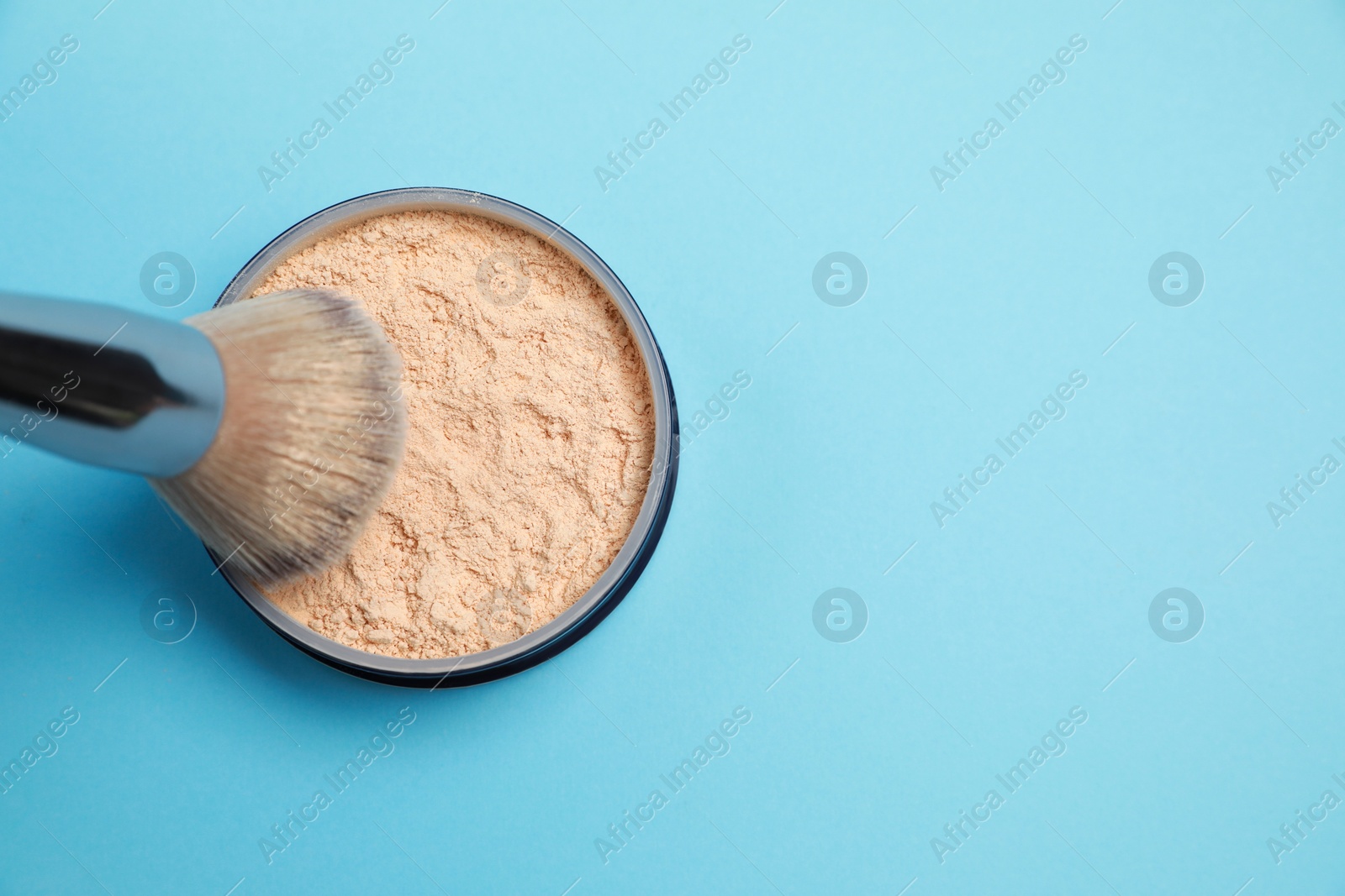 Photo of Applying face powder on brush on light blue background, top view. Space for text