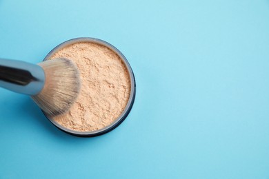 Photo of Applying face powder on brush on light blue background, top view. Space for text