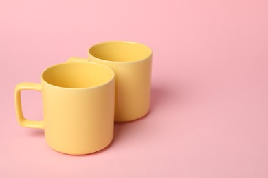 Photo of Two yellow ceramic mugs on pink background, space for text