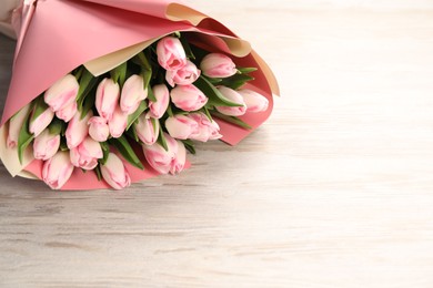 Photo of Beautiful bouquet of fresh pink tulips on light wooden table. Space for text