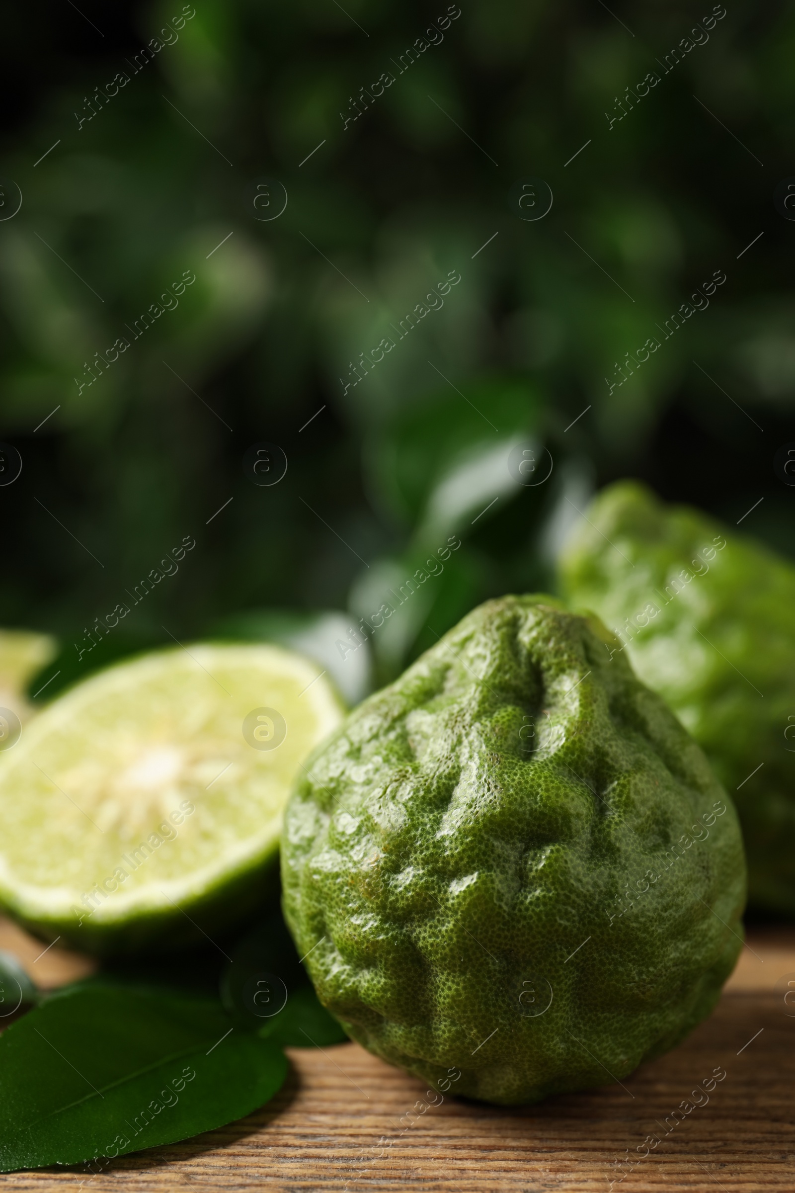 Photo of Fresh ripe bergamot fruits with green leaves on wooden table against blurred background, space for text