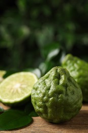 Photo of Fresh ripe bergamot fruits with green leaves on wooden table against blurred background, space for text