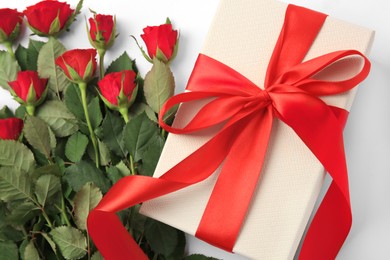 Beautiful gift box with bow and red roses on white background, top view