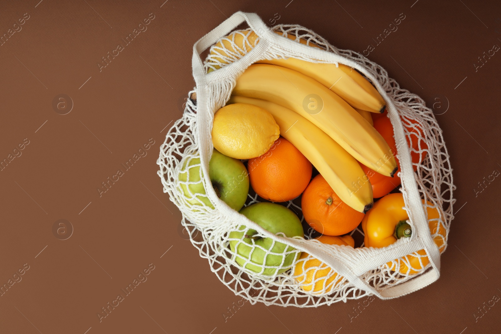 Photo of Net bag with fruits and vegetables on brown background, top view