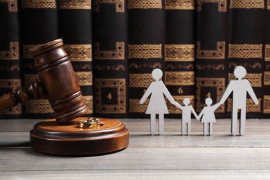 Divorce concept. Gavel, wedding rings and paper cutout of family on wooden table