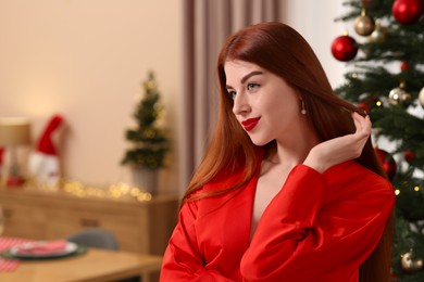 Beautiful young woman near Christmas tree at home, space for text
