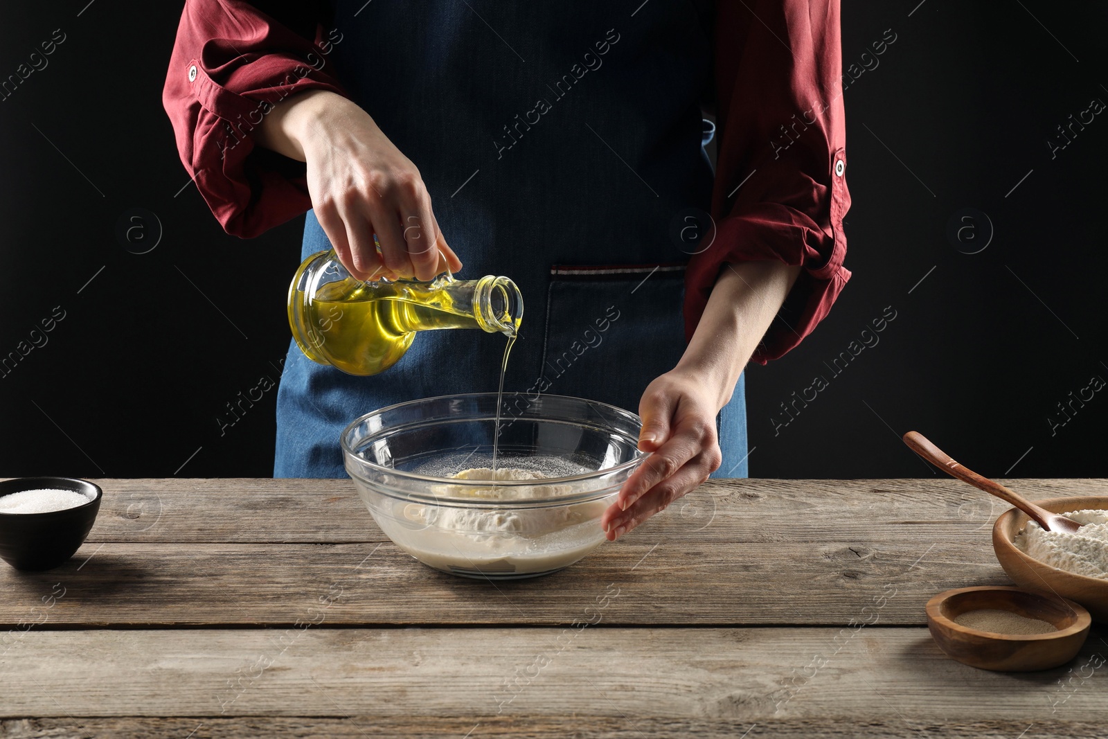 Photo of Making bread. Woman pouring oil into bowl at wooden table, closeup