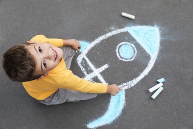 Photo of Child drawing rocket with chalk on asphalt, above view