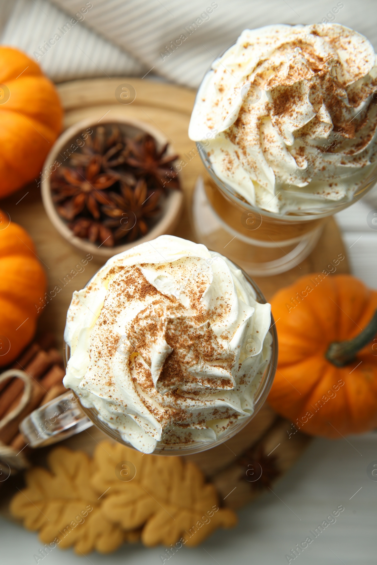 Photo of Tasty pumpkin latte with whipped cream in glasses, spices and cookies on white table, top view