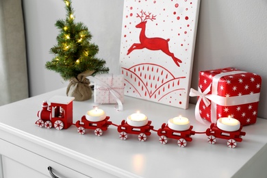 Photo of Red toy train as Christmas candle holder on white chest of drawers indoors