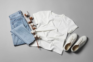 Stylish t-shirt, jeans and sneakers on light grey background, flat lay