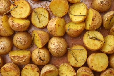 Delicious baked potatoes with rosemary as background, top view