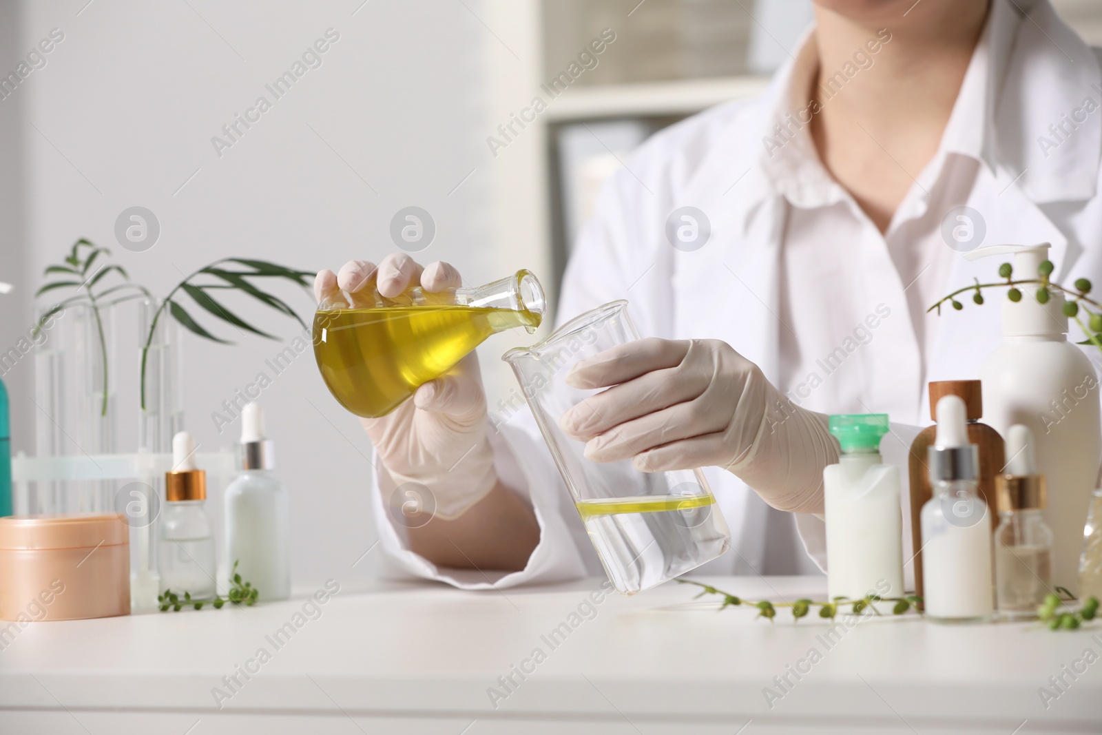 Photo of Dermatologist developing cosmetic product at white table indoors, closeup