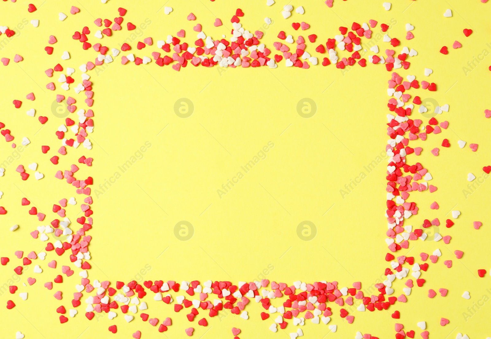 Photo of Frame made of bright heart shaped sprinkles on yellow background, flat lay. Space for text