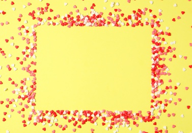 Frame made of bright heart shaped sprinkles on yellow background, flat lay. Space for text