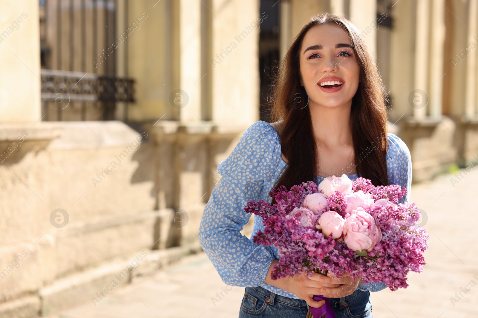 Photo of Beautiful woman with bouquet of spring flowers on city street, space for text