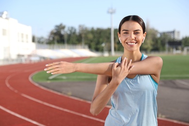 Photo of Young sportswoman with wireless earphones stretching at stadium