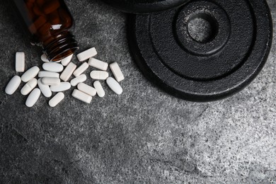 Photo of Bottle near amino acid pills and weight plates on grey table, flat lay. Space for text