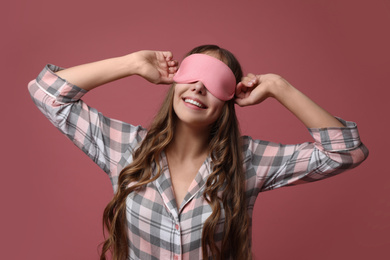 Photo of Young woman wearing pajamas and sleeping mask on dusty rose background. Bedtime