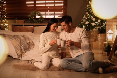 Photo of Happy couple with cups in festively decorated bedroom. Christmas celebration