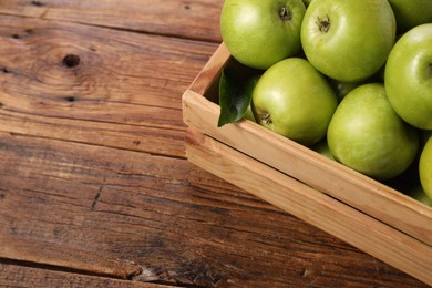 Photo of Fresh ripe green apples in crate on wooden table. Space for text