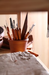 Clay and set of crafting tools on wooden rack in workshop, closeup