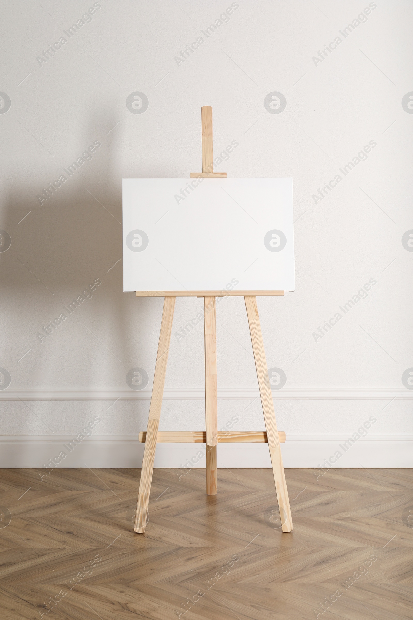 Photo of Wooden easel with blank canvas near light wall