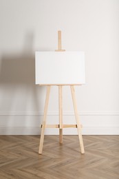 Photo of Wooden easel with blank canvas near light wall