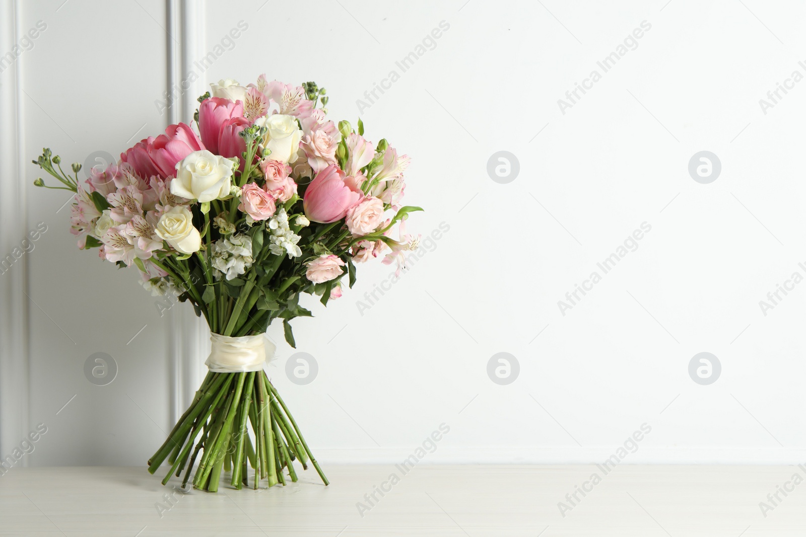 Photo of Beautiful bouquet of fresh flowers on table near white wall. Space for text