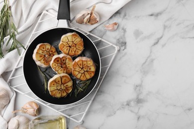 Photo of Frying pan with fried garlic, rosemary and oil on light marble table, flat lay. Space for text