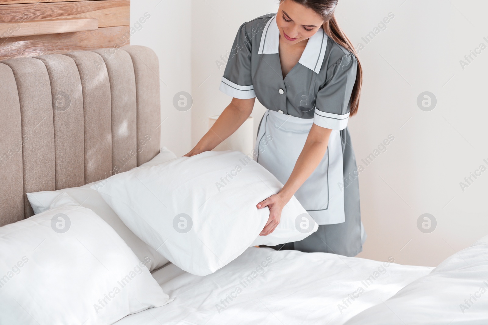 Photo of Young chambermaid making bed in hotel room