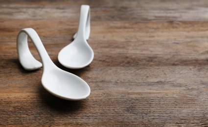 Photo of Clean empty ceramic appetizer spoons on wooden background, space for text