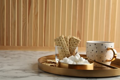 Refined sugar cubes in bowl and aromatic tea on white marble table. Space for text
