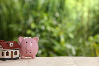 Photo of Piggy bank and little house toy on white wooden table outdoors. Space for text